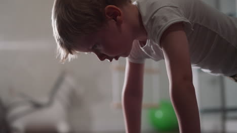 Tired-toddler-boy-tries-to-do-pushups-in-living-room-closeup