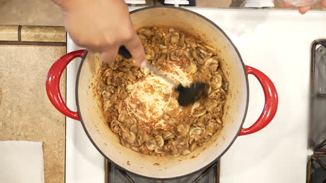 adding organic minced garlic to mushrooms sauteing on the stove and stirring them in - overhead view wild rice series