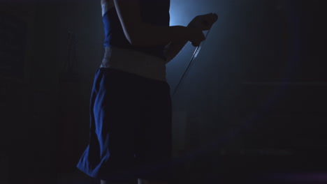 Young-beautiful-woman-professional-boxer-in-training-in-the-hall-jumps-on-a-rope-in-the-light-of-the-contra-in-a-dark-room