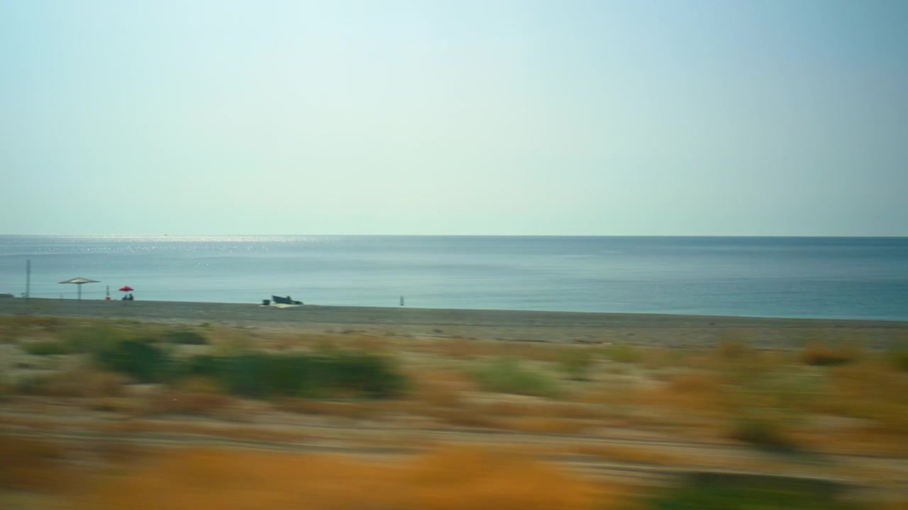 Guardando fuori dal finestrino del treno in Calabria, il mare e la spiaggia sabbiosa.