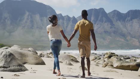 Rear-view-of-african-american-couple-holdings-hands-and-walking-at-the-beach