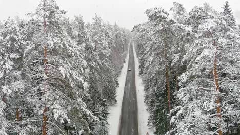 Conducción-De-Automóviles-En-La-Carretera-Forestal-De-Invierno-Durante-La-Mágica-Nevada,-Vista-Aérea