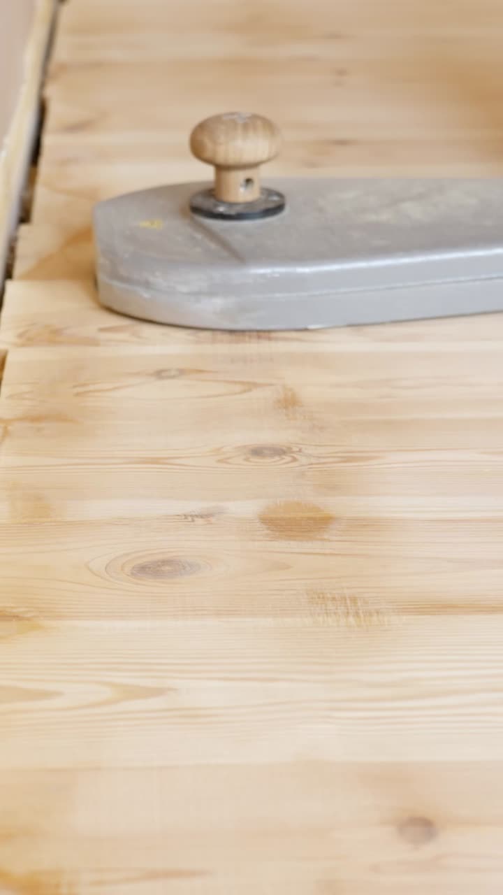 Close up of sanding machine polishing narrow edge of hardwood flooring near baseboard area, vertical