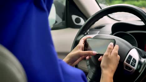 Woman in hijab texting on phone behind the self-driving steering wheel of an autonomous autopilot driverless car