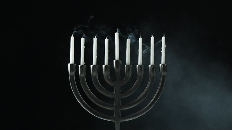 A row of nine white candles burning in a menorah are blown out, front view
