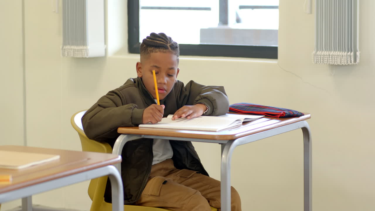 In school, young boy writing in notebook at desk, concentrating on task