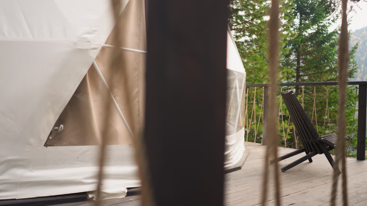 반투명한 텐트가 있는 글램핑 하우스, 관광객들이 나무 의자에 앉아 자연을 관찰할 수 있는 테라스가 있는 시골 하우스, 자연과의 연결, 로프 펜싱을 통한 전망