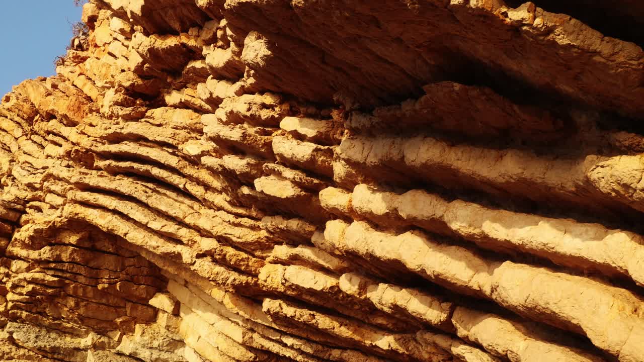 Vista panorámica de un acantilado sedimentario estratificado en Ibiza que revela estratos rocosos erosionados, una cavidad natural y cielo azul bajo la cálida luz solar mediterránea.