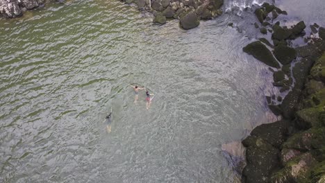 Tres-Jóvenes-Nadando-En-El-Río-Doubs,-Grandes-Rocas-Y-Musgo,-Neuchatel,-Suiza