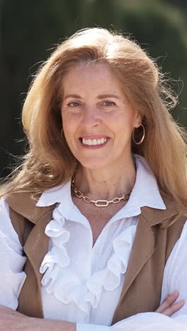 cheerful mature woman adjusting hair in city park. vertical footage
