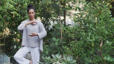 une femme biraciale pratiquant le yoga dans un jardin ensoleillé, au ralenti avec un espace de copie.