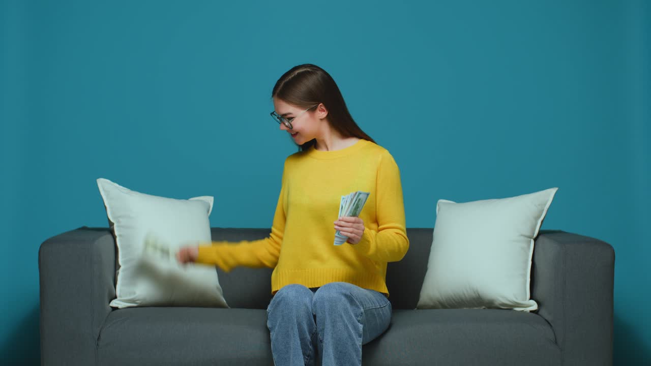 기하고 기하는 어린 소녀는 소파에 앉아 현금을 계산하고 급여 지불에 만족합니다.