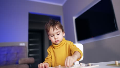 adorable little boy in yellow sweater is concentrated on puzzle game. toddler playing and studying at home.