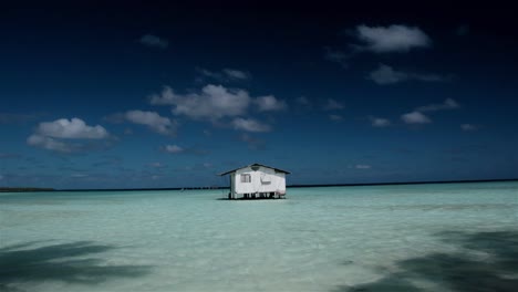a wooden hut on stilts in the crystal clear blue waters of a tropical island atoll in the remote south pacific tuamoto region of french polynesia