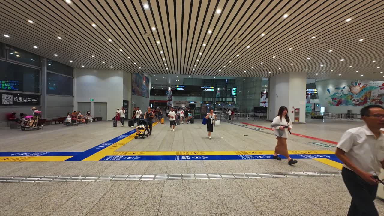 People walk through the brightly lit interior of Guangzhou airport, carrying luggage.