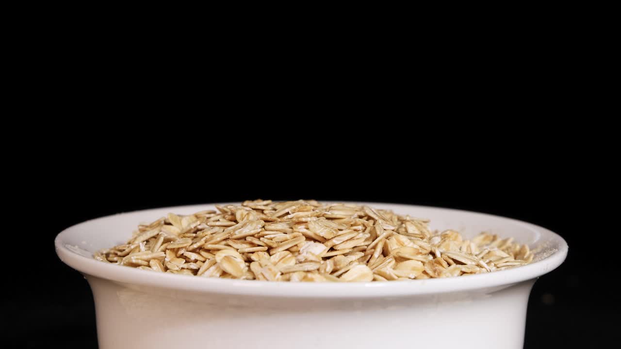 A spoon drops toasted corn cereal into a white bowl against a black background, highlighting the cereal's texture and motion