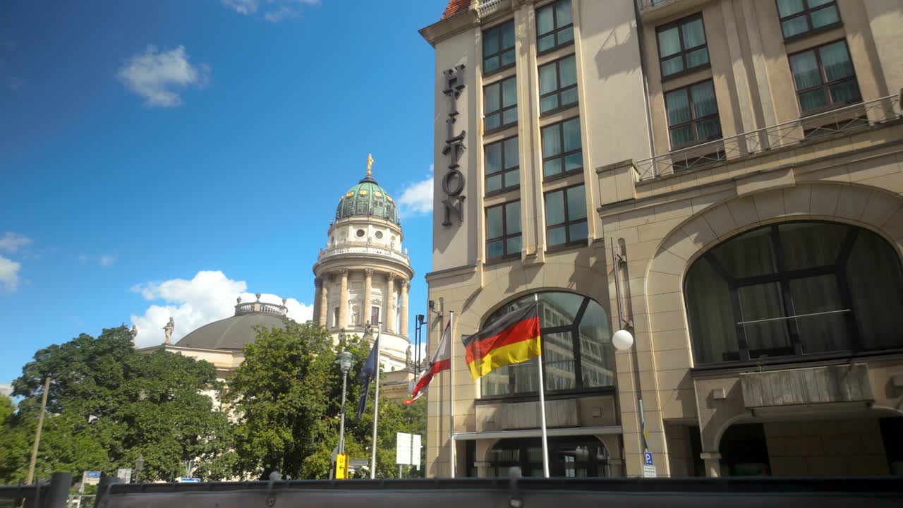Front view of Berlin's Hilton hotel with German and Austrian flags beside historic Gendarmenmarkt cathedral