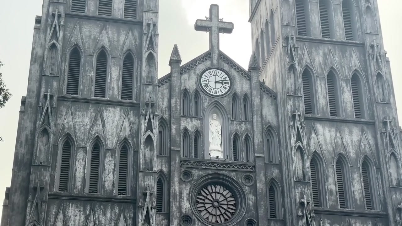 Vista ravvicinata della facciata della Cattedrale di San Giuseppe ad Hanoi, che evidenzia l'intricata architettura neogotica, l'orologio centrale, il rosone, le aperture ad arco e le decorazioni in pietra sotto un cielo coperto.