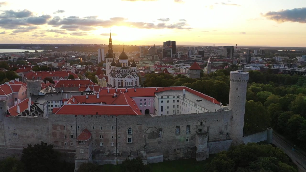 Filmato mozzafiato con drone del Centro Storico medievale di Tallinn al tramonto. L'inquadratura mostra la Collina di Toompea, la Cattedrale di Santa Maria e gli edifici dai tetti rossi sotto un cielo drammatico di nuvole rosa e arancioni.