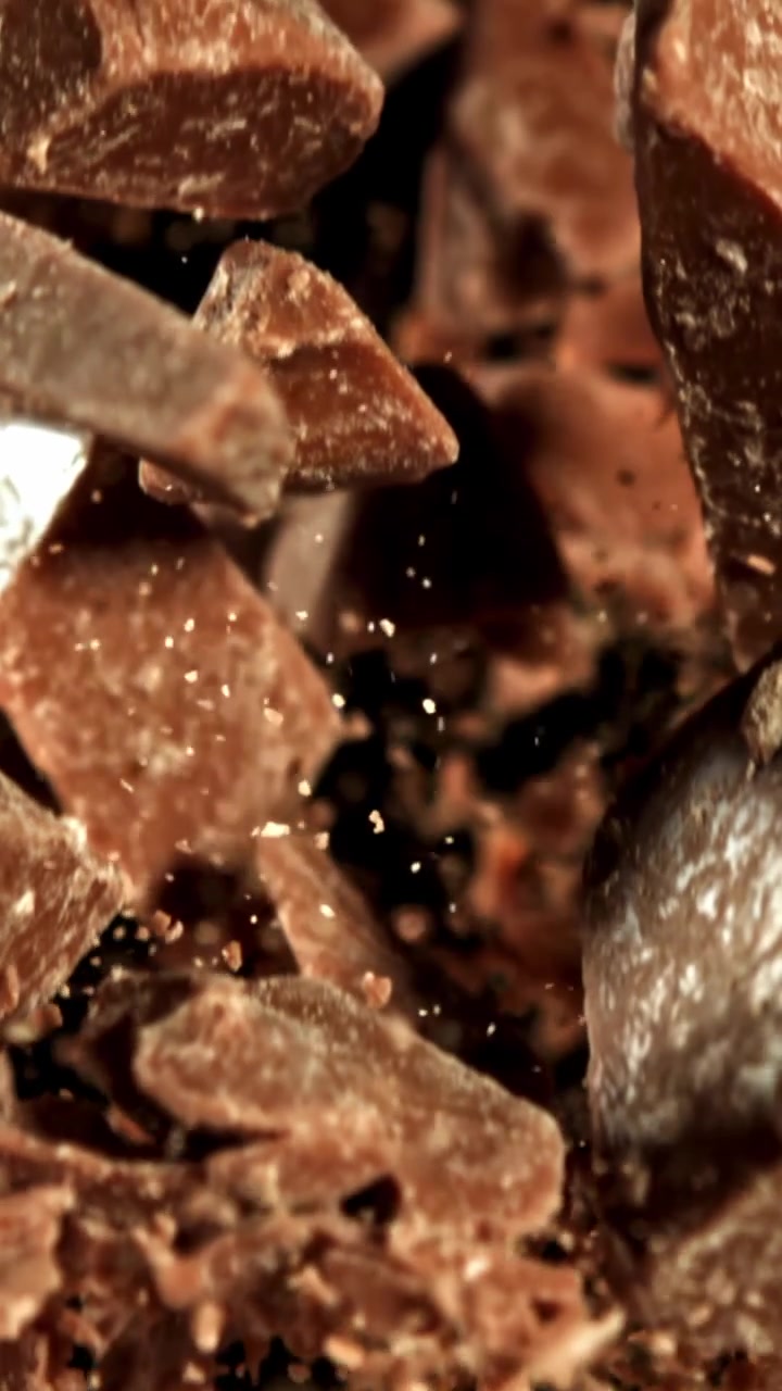 Slow Motion of Chocolate Chunks and Dust Falling on Black Background