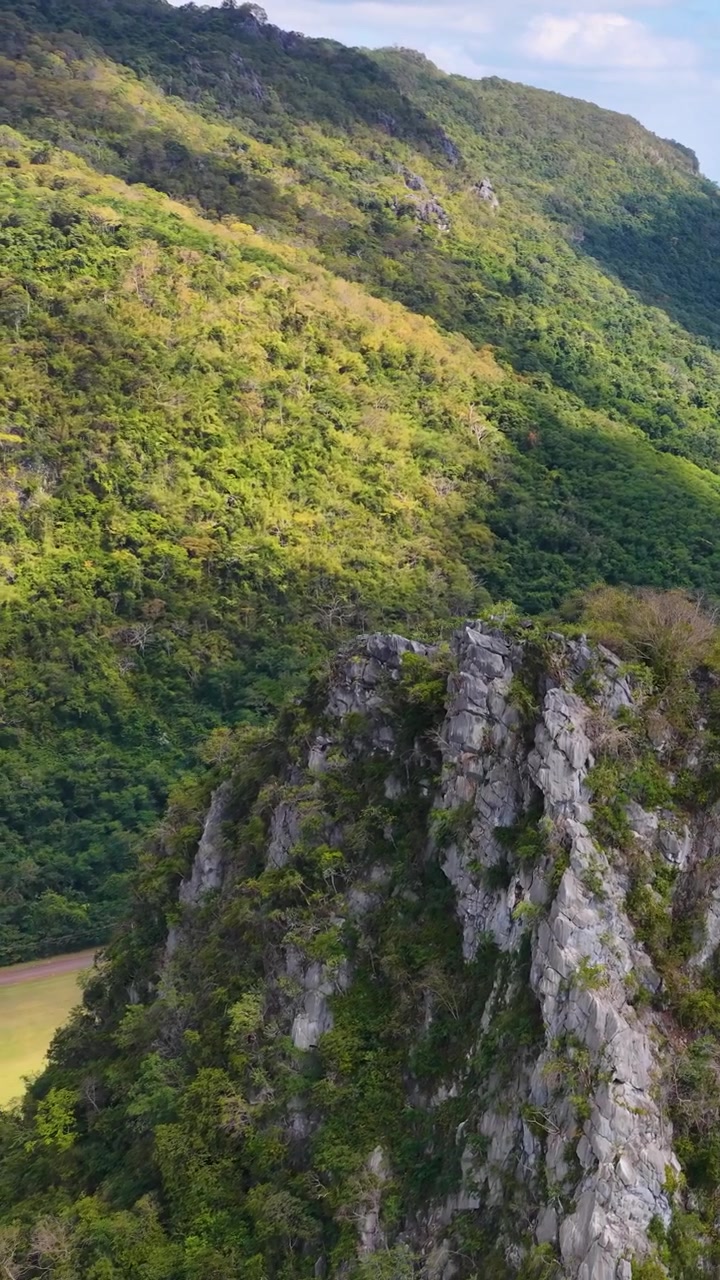 Riprese con drone rivelano aspre scogliere calcaree che si ergono sopra una fitta foresta tropicale sotto la luce intensa del sole.