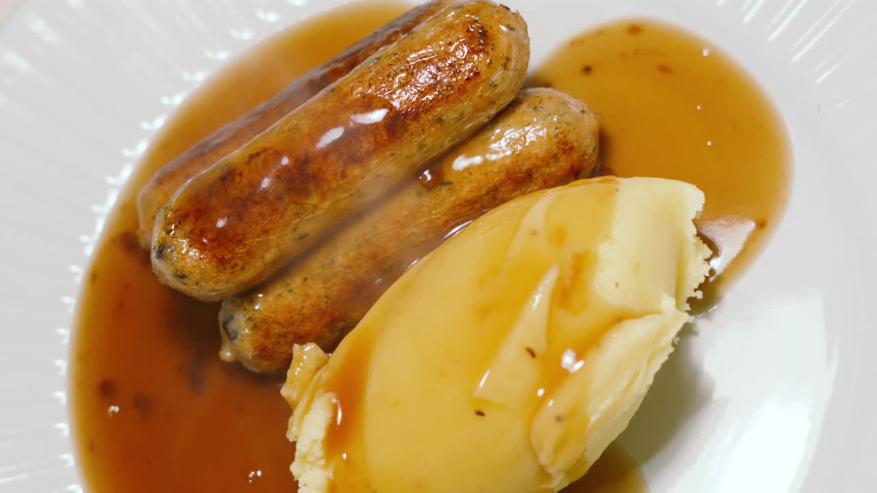 Ylhäältä otettu kuva perinteisestä brittiläisestä pubiruoasta, jossa on vegaanisia makkaroita, perunamuusia ja täyteläistä kastiketta. Täydellinen ruoanlaitto- tai lifestyle-sisältöön