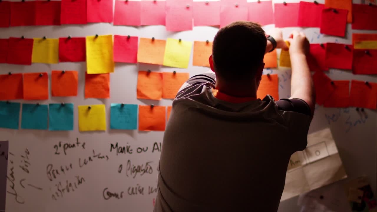 el hombre examina la nota pegajosa durante la tormenta de ideas y la vuelve a colocar.