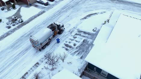 orbiting aerial view of a public utility truck picking up trash on a snowy day