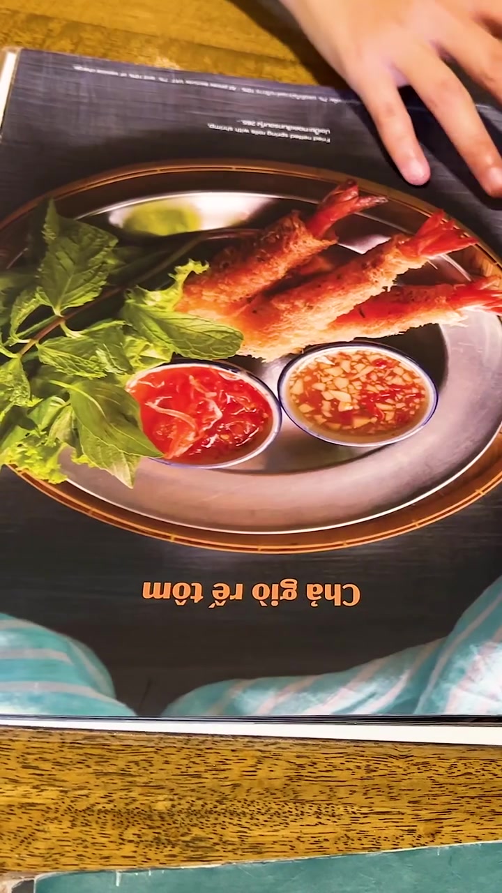 Hænder bladrer igennem en farverig vietnamesisk restaurantmenu, der viser forskellige retter frem i et veloplyst miljø