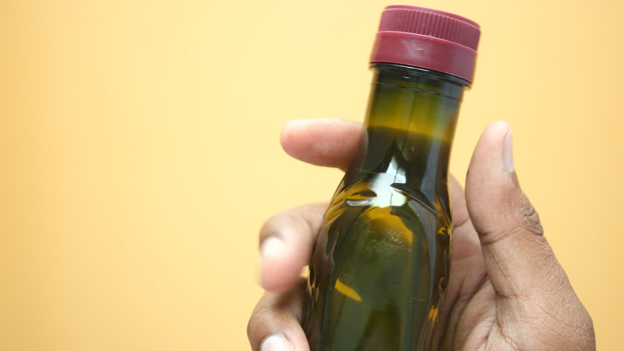 Hand holding a small dark green glass bottle with a red cap
