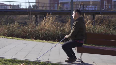 blind man sitting on a park bench. he gets up and walks.