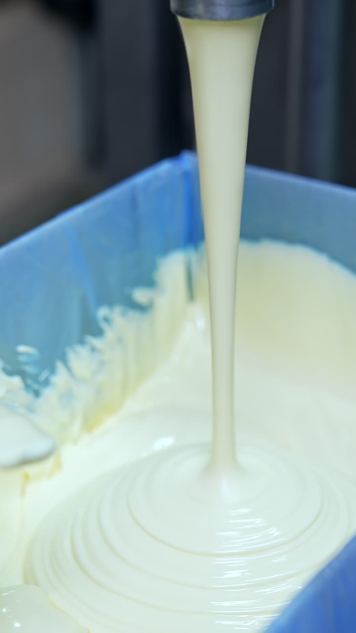 Factory for butter production. Creamy white dairy product pouring into box. Making fresh butter on a milk farm. Dairy product manufacturer. Hand of worker is mixing butter. Close-up.. Vertical video
