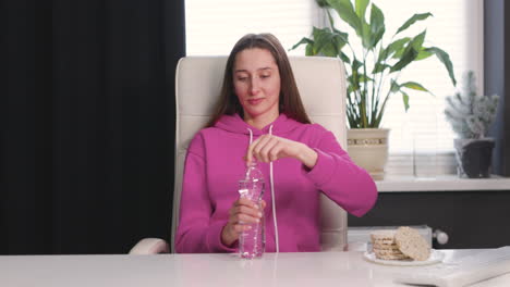 happy young woman sitting at desk and drinking water from a plastic bottle