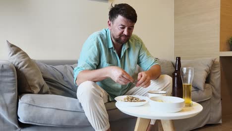 man relaxing on sofa with beer and snacks