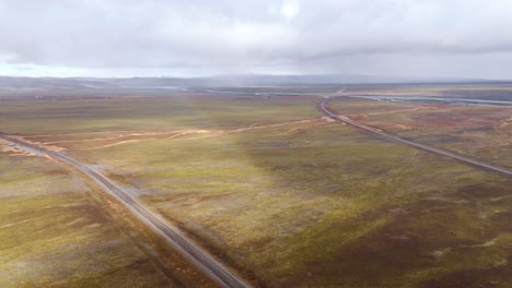 an empty road winding through colorful icelandic moorland under overcast skies, vast and remote, aerial view