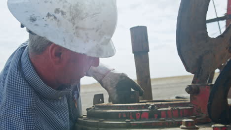 mid-aged caucasian worker wearing protective helmet works with equipment. preparation of the machines for drilling oil.