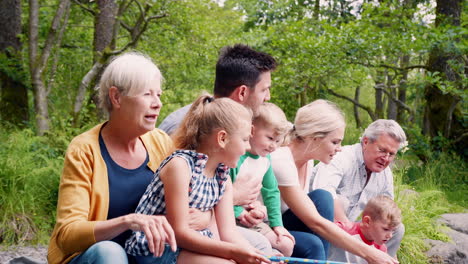 Zeitlupenaufnahme-Einer-Familie-Aus-Mehreren-Generationen,-Die-Auf-Felsen-Sitzt-Und-Mit-Netzen-Im-Fluss-Im-Britischen-Seengebiet-Fischt