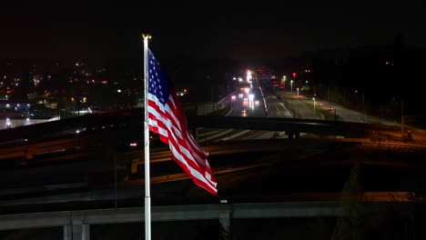 american flag with cars driving through the highway in the background at night