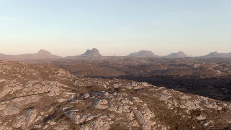 Aerial view flying over a remote rocky area of Assynt towards the famous mountains of Canisp, Suilven, C&ugrave;l M&ograve;r and Stac Pollaidh on a sunny spring evening