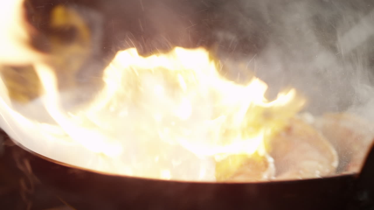 close-up handheld shot of large shrimp cooking in a pan over fire with flames, steam rising in the kitchen.