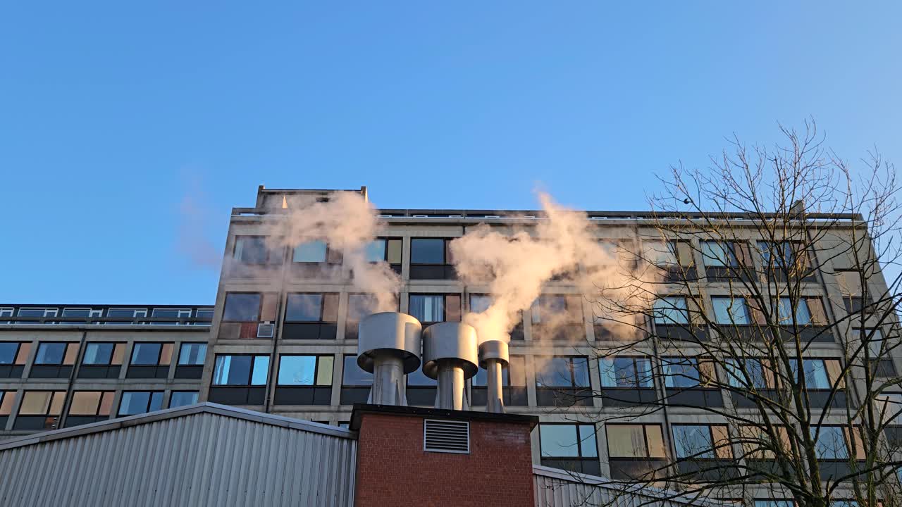 Steam rises from metal boiler exhaust stacks on a residential building, showing winter heating demand and pollution