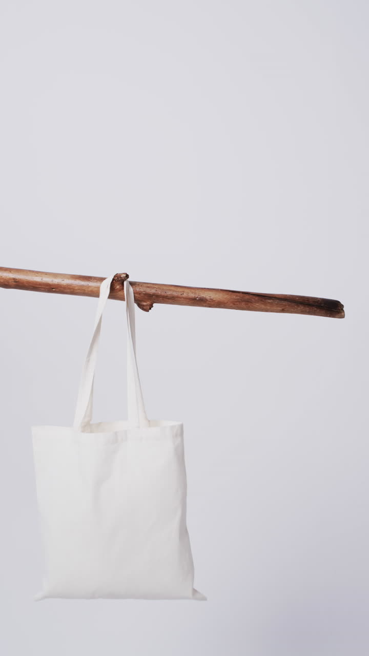 Vertical video of white canvas bag hanging from branch with copy space on white background