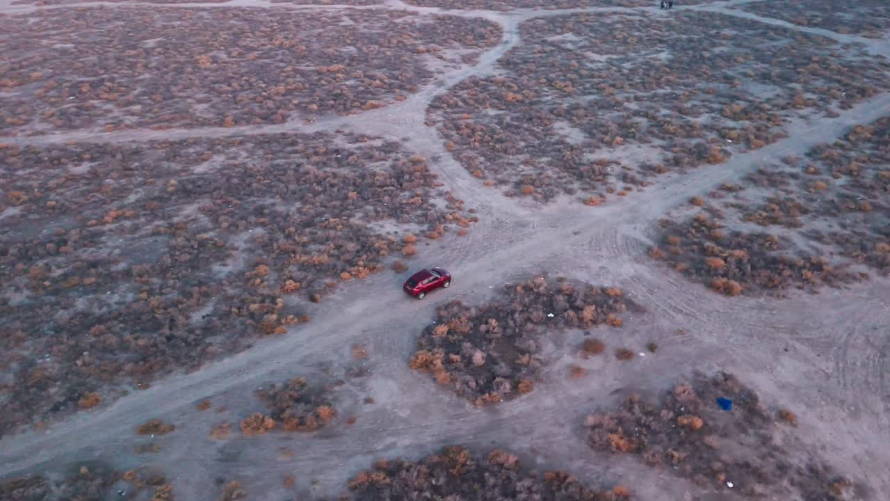 High drone view of a red car on dusty desert crossroads with branching trails at twilight—cinematic road-trip off-road establishing plate; empty landscape, no people