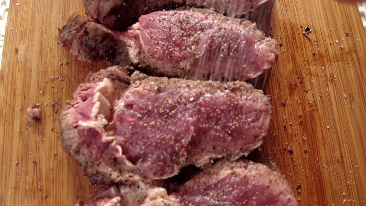Close up of a man seasoning pieces of cooked beef on a wooden cutting board