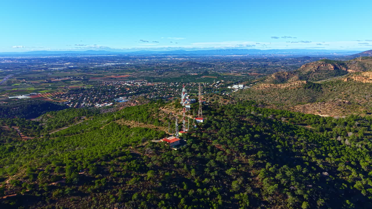Vedute dalla cima di una collina che si affaccia su un'area rurale con torri di comunicazione e vegetazione in lontananza durante una giornata di sole