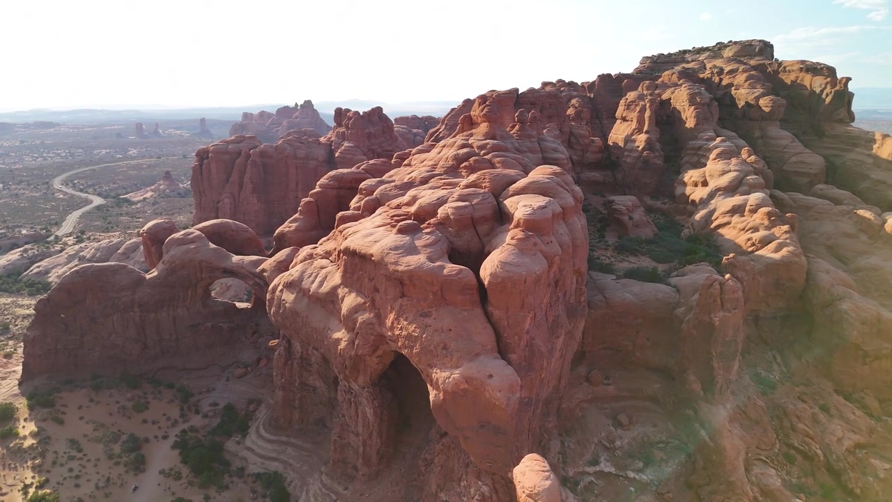 Splendido filmato stock del Parco Nazionale di Arches, USA, durante un pomeriggio luminoso. La luce solare brillante illumina le maestose strutture di arenaria rossa e il paesaggio desertico sotto un cielo azzurro limpido.