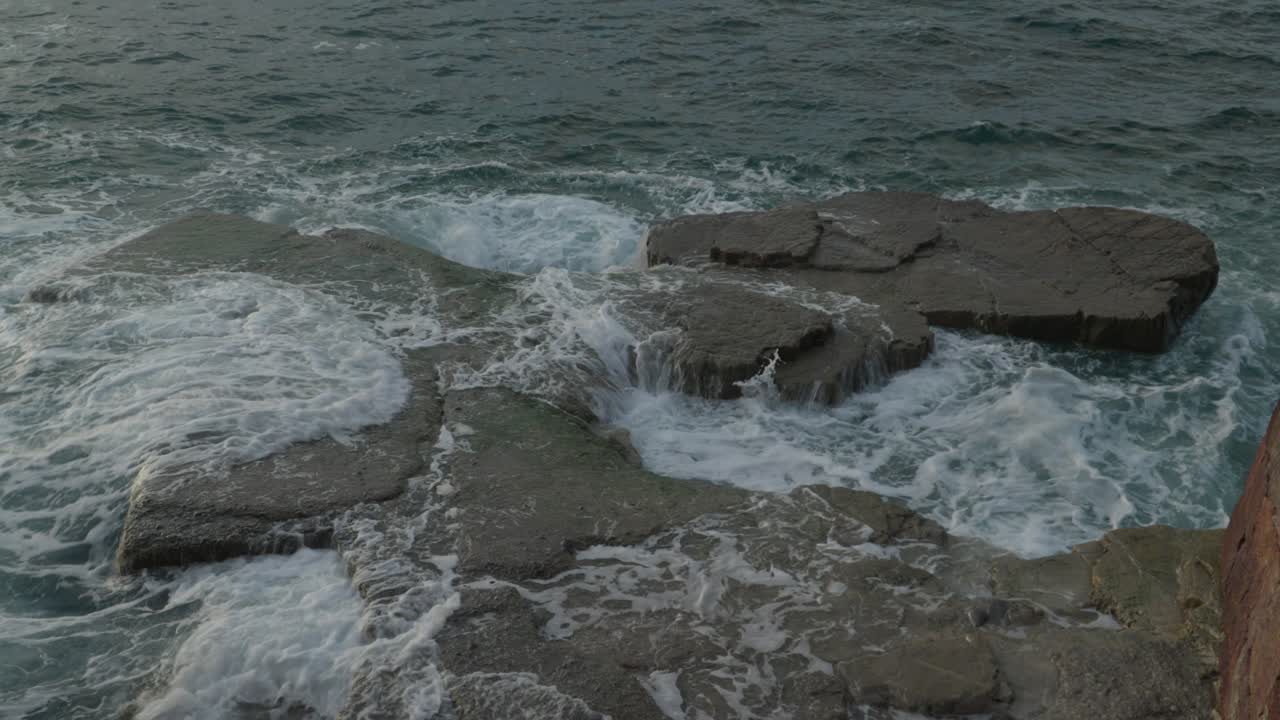 Potenti onde oceaniche si infrangono e si schiantano su scure formazioni rocciose costiere lungo l'aspra costa di Gijon, Spagna. Paesaggio marino drammatico con schiuma bianca e acqua turbolenta