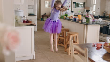 happy ballerina girl dancing in kitchen having fun practicing ballet dance moves wearing purple tutu at home