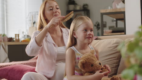 happy pregnant mother brushing hair of little daughter