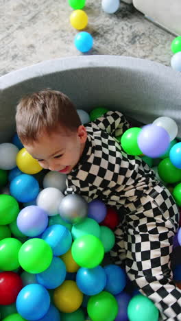 little baby lies in a dry pool covered by plastic balls. happy toddler sits up smiling happily. top view. vertical video.